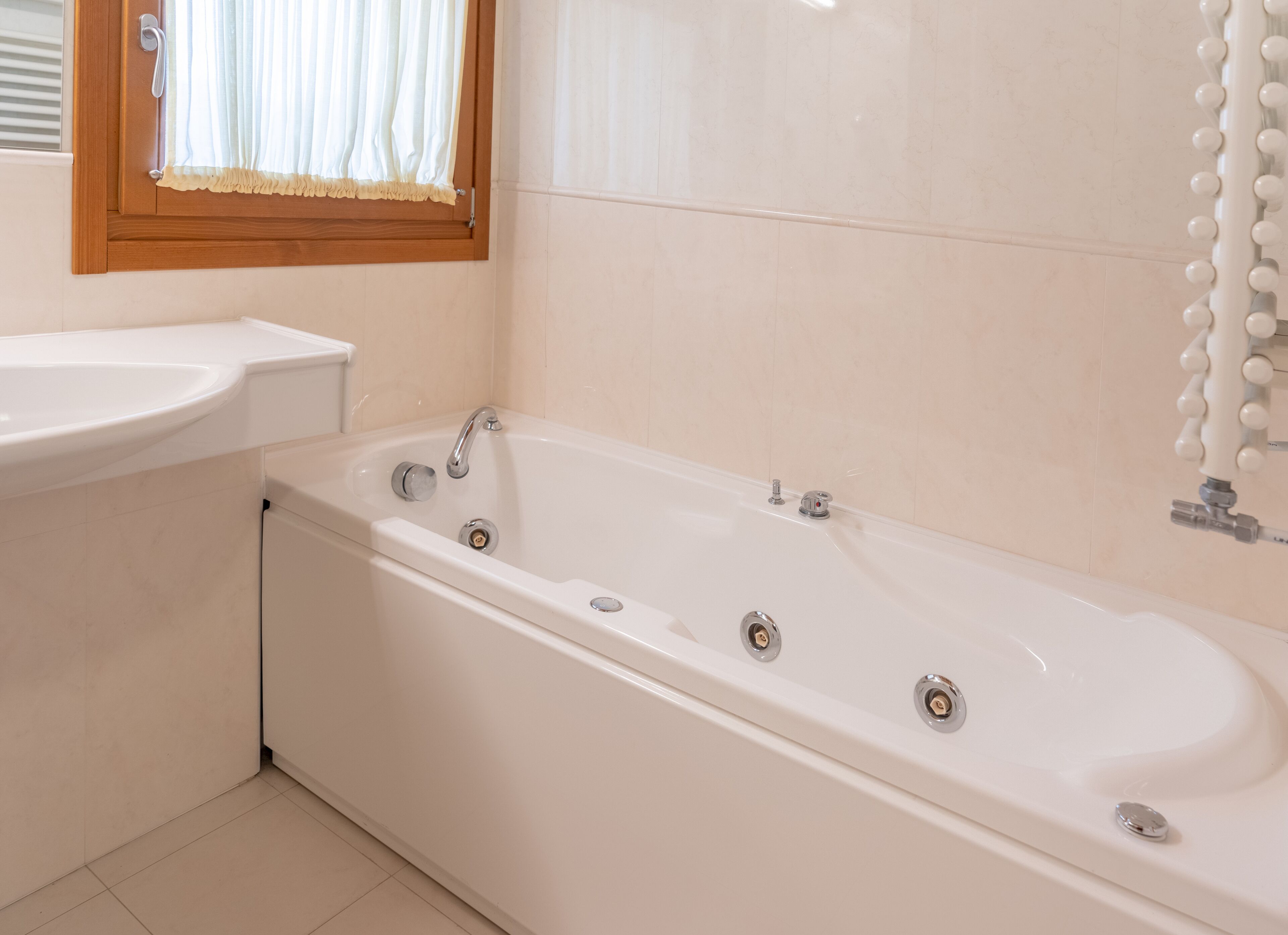 Ein modernes Badezimmer mit einer freistehenden Badewanne, einem Waschbecken und einem Fenster mit Vorhängen.
