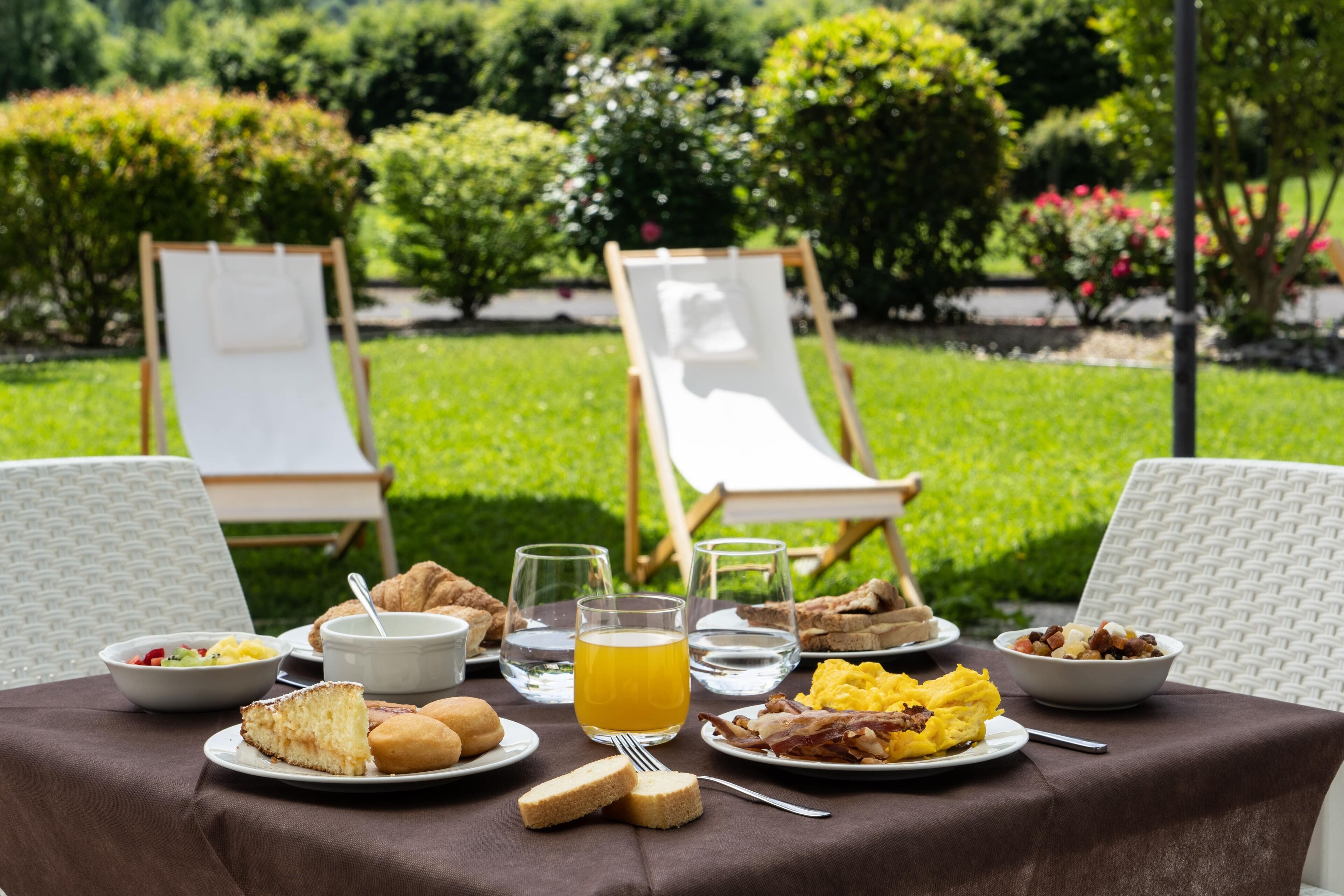 Een ontbijt buiten, met een gedekte tafel voor twee personen, inclusief borden met eten, drinken en twee loungestoelen.