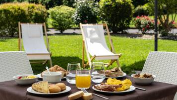 Een ontbijt buiten, met een gedekte tafel voor twee personen, inclusief borden met eten, drinken en twee loungestoelen.