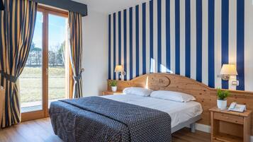 Un dormitorio con una cama grande, cabecera de madera, dos mesitas de noche con lámparas, una ventana con cortinas y vistas al exterior.