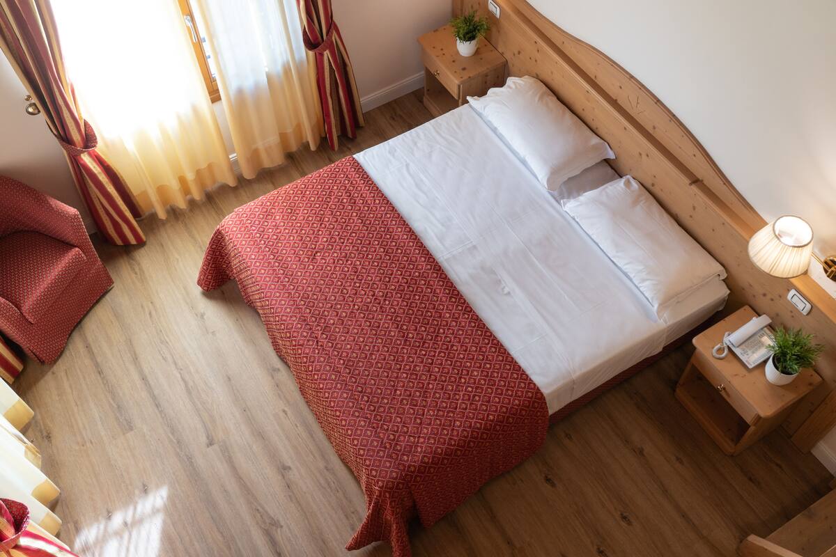A neatly made bed with a patterned bedspread, a wooden headboard, a bedside table with a lamp, and a small plant.
