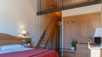 Une chambre à coucher comprenant un lit, une table de chevet, une lampe, une armoire en bois, un bureau avec une chaise et un escalier menant à l’étage supérieur.