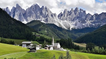 Un pueblo de montaña con una iglesia y varias construcciones, rodeado de campos verdes exuberantes y altas montañas.