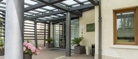 A covered outdoor area with a glass roof, potted plants, and a sign for Hotel Canova.