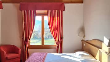 Une chambre avec un plafond en bois, un lit recouvert de draps blancs, un fauteuil rouge et une fenêtre avec des rideaux.