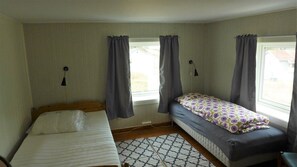 A small room with two beds, a window with curtains, a wall-mounted lamp, and a patterned rug. - Skrolsvik Kystferie (Senja)