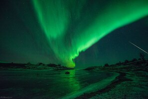 A nighttime landscape with a river, a road, and a green aurora display. - Skrolsvik Kystferie (Senja)