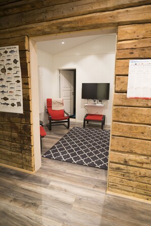 A room with a wooden floor, a red chair, a black and white patterned rug, a television on a stand, and a wooden wall with a poster.