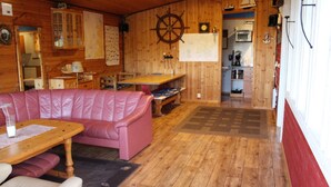 Interior acogedor de una cabaña, con detalles de madera, un sofá de cuero rosa, una mesa de comedor de madera y una zona de cocina al fondo.