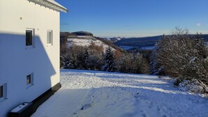 A snow-covered landscape with a white building featuring multiple windows and a chimney. - Appart-Hotel Harmonie (Winterberg)