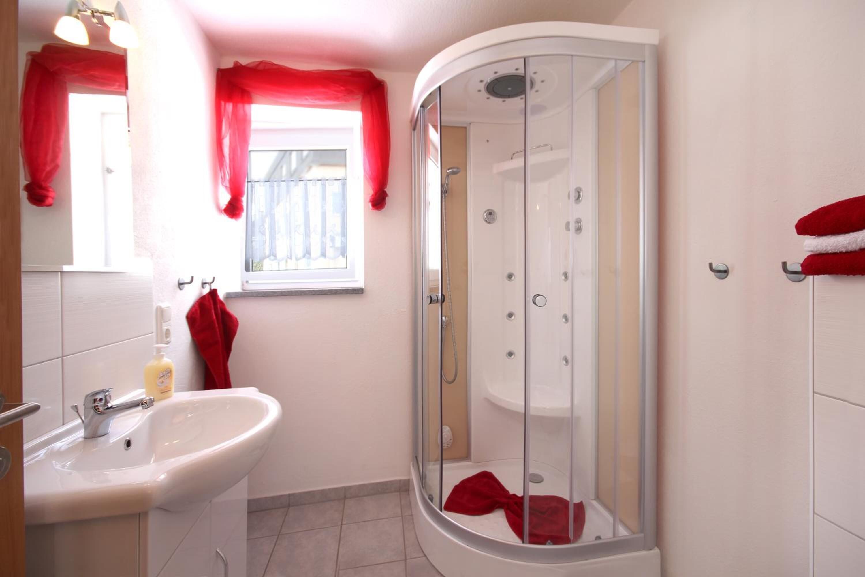Ein Badezimmer mit einem weißen Waschbecken, einer Duschkabine und roten Vorhängen.