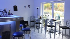 A bar area with stools, a table, and chairs. There is a window with a view of cars and trees. - Appart-Hotel Harmonie (Winterberg)