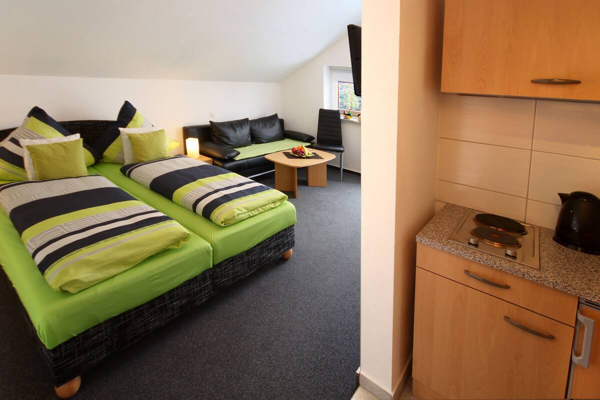 Une chambre d’hôtel avec deux lits, un petit canapé, une table ronde et un coin cuisine.