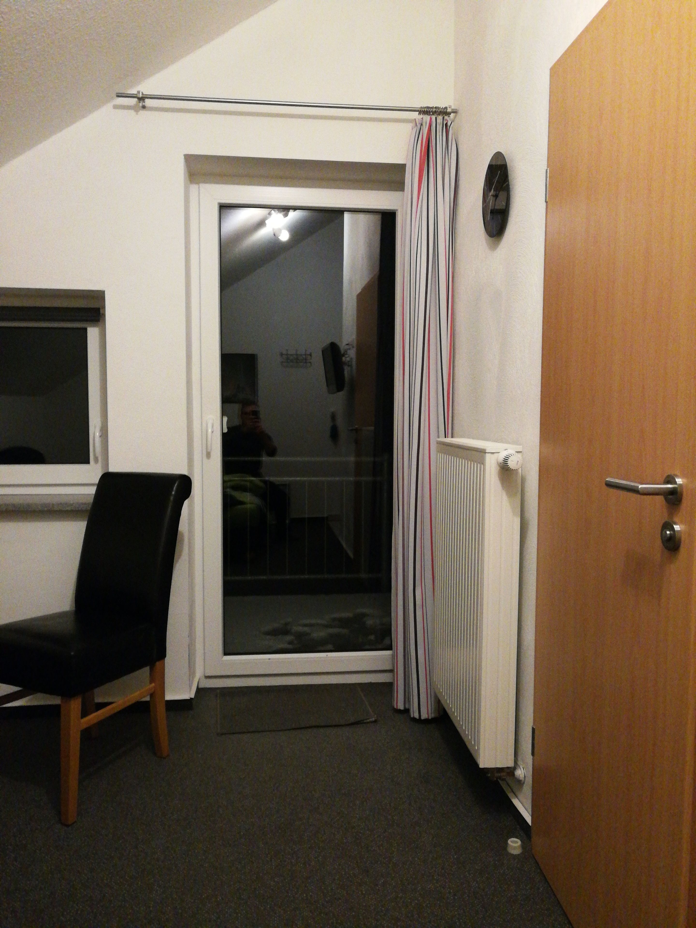 A room with a black chair, a door, a radiator, and a window.