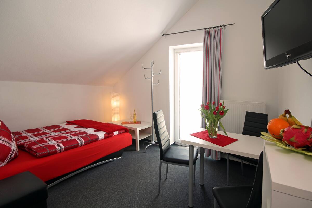 Une chambre d’hôtel avec un lit, un bureau, une chaise, une télévision et une fenêtre avec des rideaux.