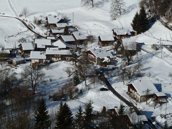 A snow-covered village with traditional wooden houses, a winding road, and sparse trees.