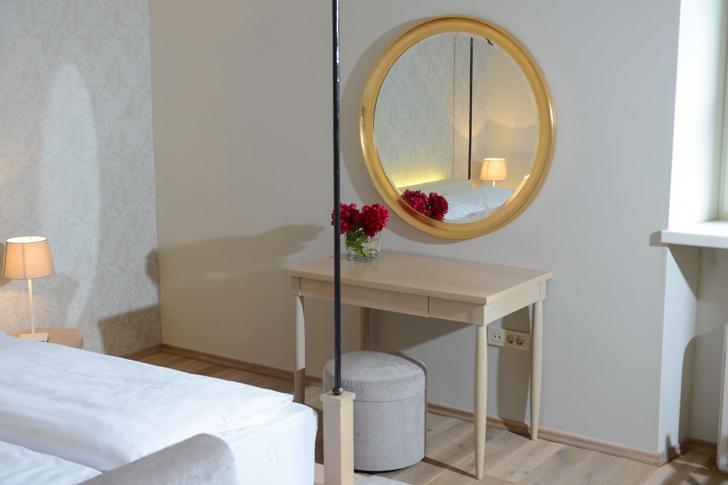 Una camera d'albergo con un letto, una scrivania con uno specchio, uno sgabello e una lampada.