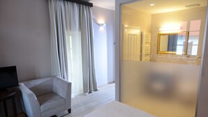 Habitación de hotel con cama, sofá, televisor y baño con espejo y toallero.