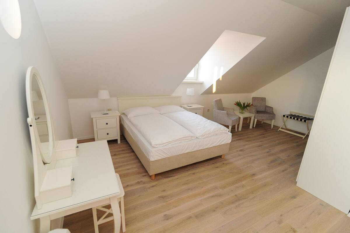 Une chambre à coucher avec un lit, un bureau doté d’un miroir, une chaise, une petite table et une lampe.