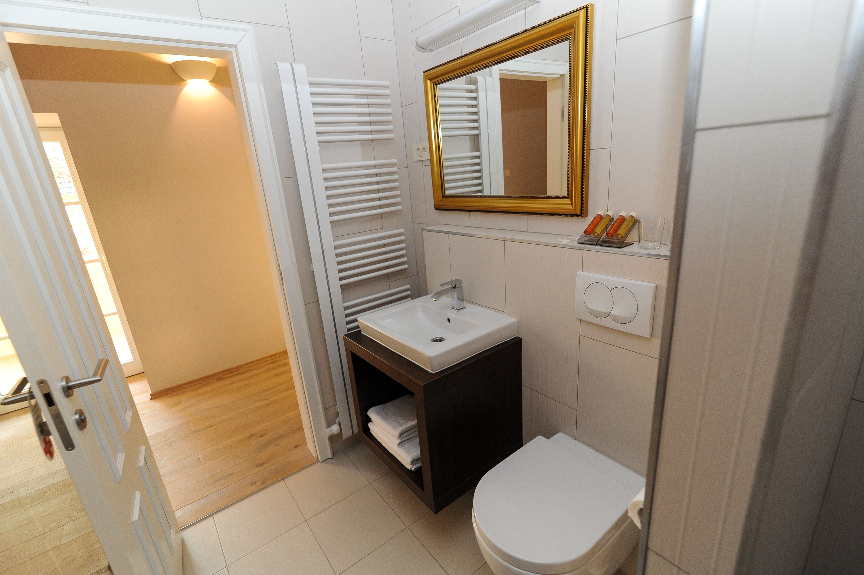 A bathroom with a white sink, a toilet, a mirror with a gold frame, and a towel rack.
