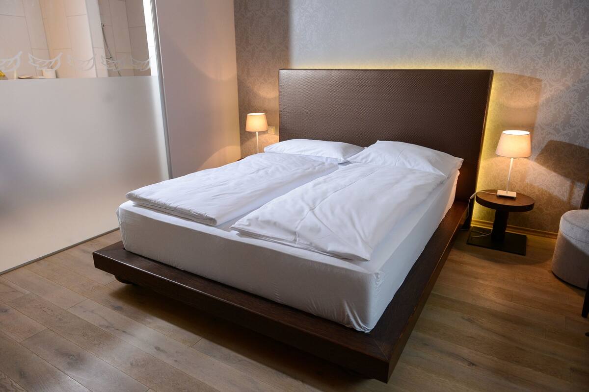 Un lit bien fait, avec du linge de lit blanc, une tête de lit en bois et deux lampes de chevet.