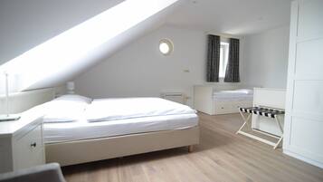 A bedroom with a sloped ceiling, a bed, a bedside table, a chair, a wardrobe, and a window with curtains.