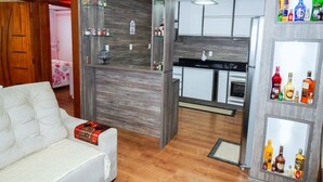 A modern living room with a white sofa, a wooden partition, and a kitchen area with cabinets and a countertop. - Casa Charm Gramado (Gramado)