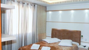 A hotel room with a bed, a nightstand, a wall-mounted light, and a curtain. - Casa Charm Gramado (Gramado)