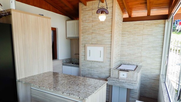 A compact kitchen with granite countertops, wooden cabinets, and a stone backsplash. - Casa Charm Gramado (Gramado)