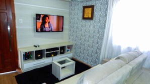 A living room with a flat-screen TV mounted on the wall, a sofa, a coffee table, and a TV stand with shelves. - Casa Charm Gramado (Gramado)