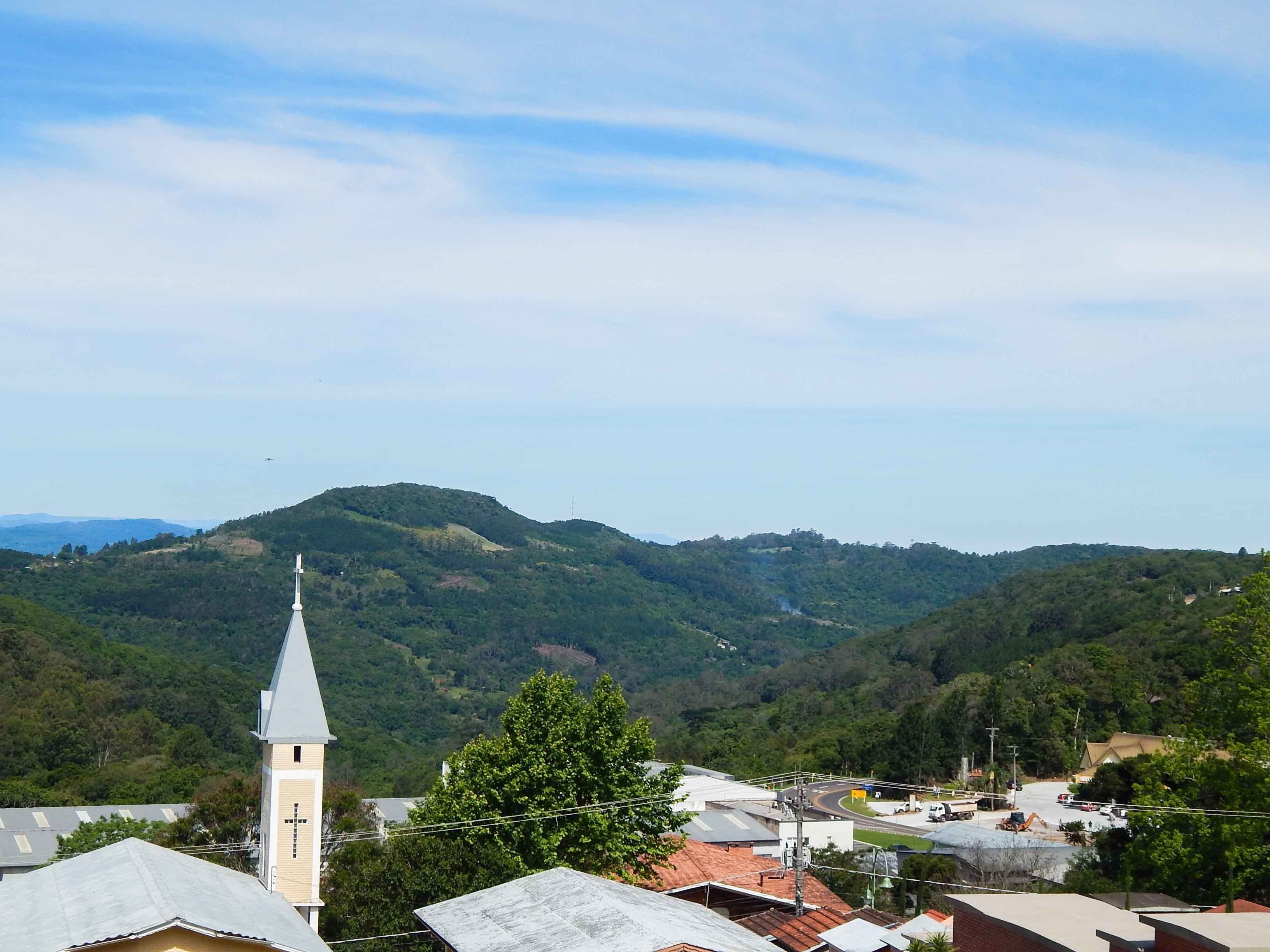 Una iglesia con un campanario alto, rodeada de edificios residenciales y colinas verdes exuberantes al fondo.