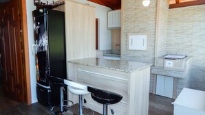 A modern kitchen with a central island, bar stools, and a ship model on the refrigerator. - Casa Charm Gramado (Gramado)