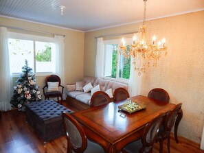 A dining area with a wooden table, chairs, a chandelier, a Christmas tree, and a sofa with cushions.