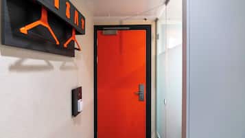 Un pasillo con una puerta roja, un perchero con ganchos naranjas y un interruptor de luz en la pared.