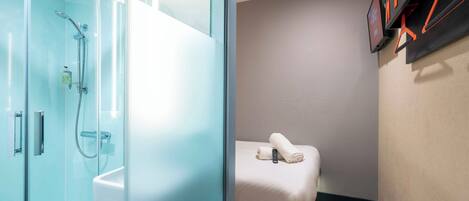 A modern bathroom with a glass shower enclosure, a white sink, and a towel on a bench.