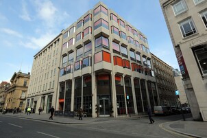 Un edificio de varios pisos con un diseño arquitectónico moderno, que cuenta con amplios ventanales y una entrada a nivel de calle.