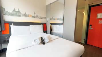 Une chambre d’hôtel avec un lit, une fresque représentant un paysage urbain, une porte rouge et un miroir.