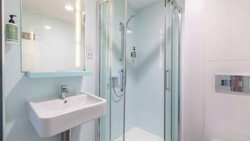 Un baño moderno con ducha envuelta en vidrio, un lavabo blanco y un espejo.
