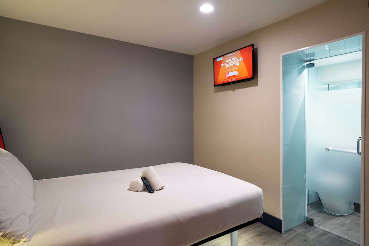 A hotel room with a bed, a television mounted on the wall, and a glass shower enclosure.