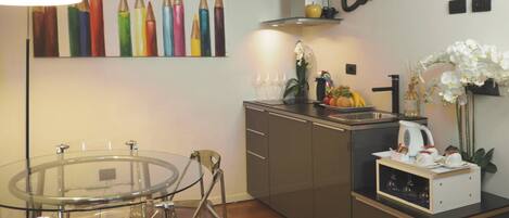 Een moderne keuken met een glazen eettafel, roestvrijstalen apparatuur en een decoratief kunstwerk.