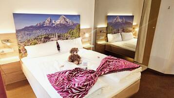Hotelkamer met een bed, een teddybeer, een spiegel en een schilderij met uitzicht op bergen.