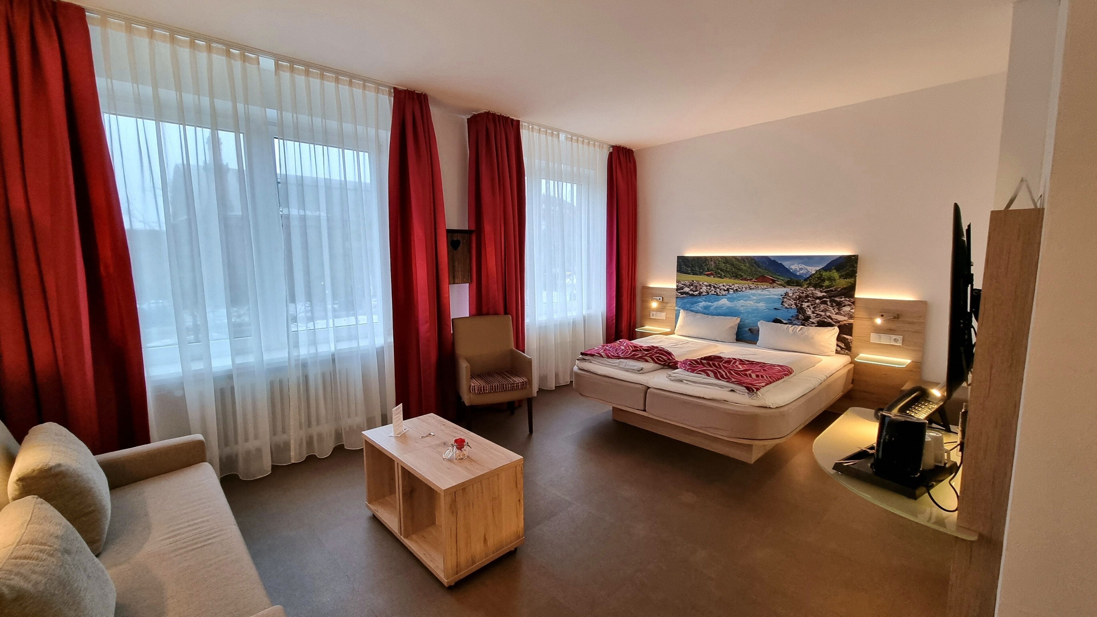 Una habitación de hotel con cama, escritorio, silla, una mesita y un cuadro en la pared.
