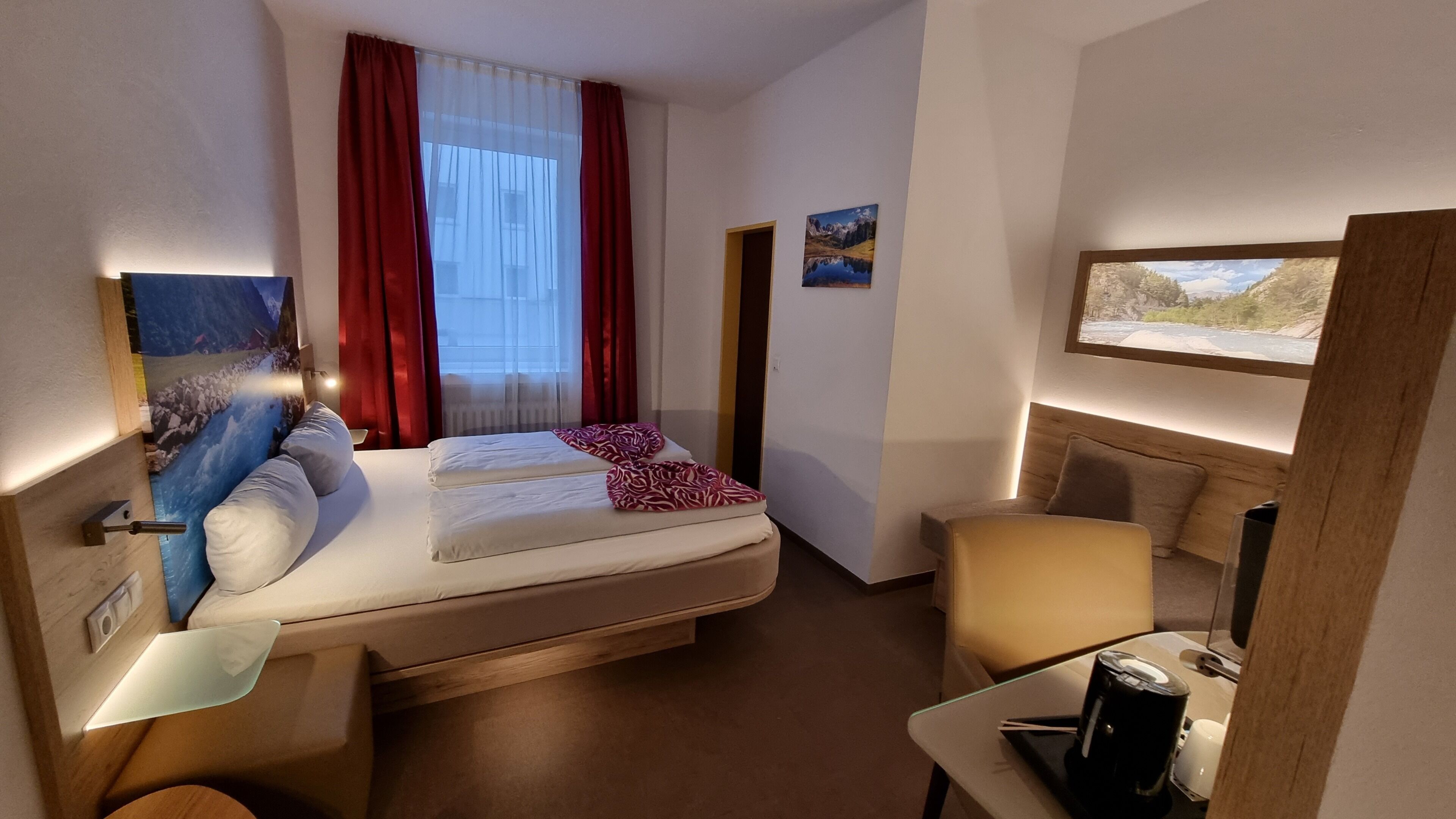 Una camera d'albergo con un letto, una scrivania, una sedia, un quadro e una finestra con tende.