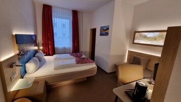 Una camera d'albergo con un letto, una scrivania, una sedia, un quadro e una finestra con tende.