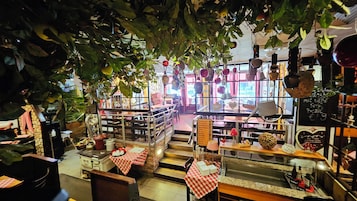 An indoor restaurant with tables and chairs, a counter with food items, and hanging decorations.