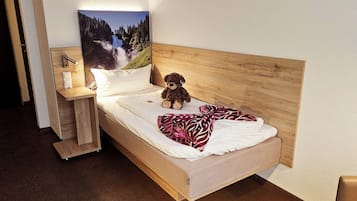 A single bed with a wooden headboard, a teddy bear, a blanket, and a nightstand with a lamp.