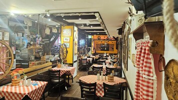 Interno di un ristorante con diversi tavoli e sedie, una grande ruota di legno e vari oggetti appesi.