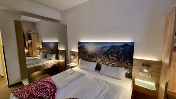 Habitación de hotel con una cama grande, un espejo y un cuadro colgado en la pared de un paisaje montañoso.