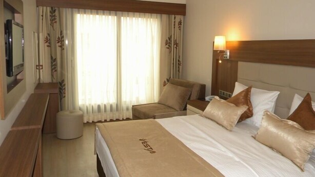 A hotel room with a bed, two chairs, a TV, and a lamp. - Vesta Fuar Hotel (Izmir)