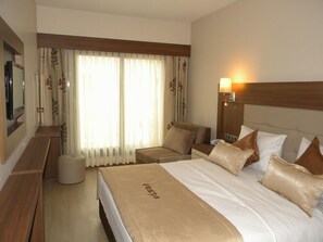 Una habitación de hotel con una cama, dos sillas, un televisor y una lámpara.